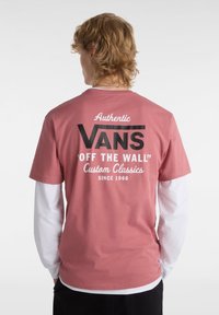 Camiseta de algodón rosa con un gráfico negro que incluye el texto "VANS", "OFF THE WALL" y "Custom Classics" en la parte posterior. Mangas cortas.