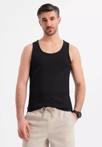 Svart ribbat linne med bred u-ringning, figurnära design. Modellen bär ljusbeiga shorts och en svart klocka. En enkel och avslappnad look.