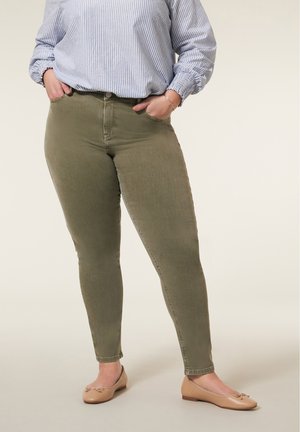 Olijfgroene skinny jeans met een zachte textuur, een strakke pasvorm en een klassieke vijf-pocketstijl. Gecombineerd met lichtbeige platte schoenen.