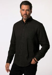 Camisa de botón negra texturizada con rayas verticales, mangas largas y un bolsillo en el pecho, combinada con pantalones negros.