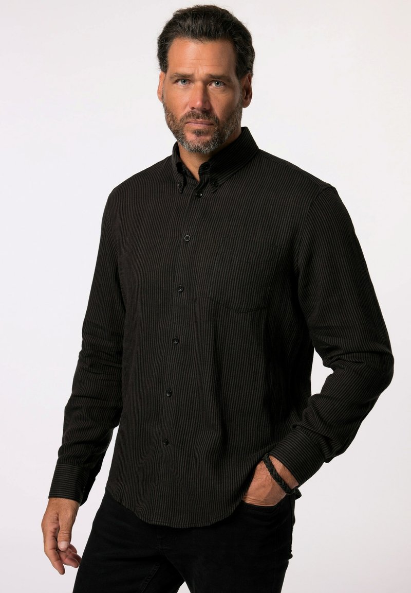 Camisa de botón negra texturizada con rayas verticales, mangas largas y un bolsillo en el pecho, combinada con pantalones negros.