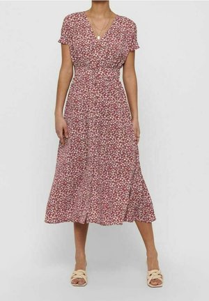 Kobieta w czerwonej kwiecistej sukience midi z krótkimi rękawami, dekoltem w serek i marszczoną talią, w połączeniu z beżowymi plecionymi sandałami z odkrytymi palcami.