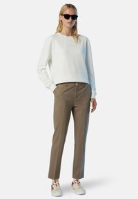 Felpa bianca con logo, pantaloni beige e sneakers bianchi con accenti rossi. Tessuto morbido, design aderente e tasche sui pantaloni.