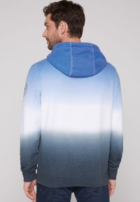 Felpa con cappuccio blu a degradé con una texture morbida, dotata di cappuccio con cordino e polsini a coste, che passa da un blu chiaro a un blu scuro.