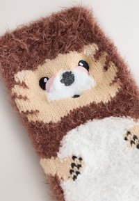 Calzino lavorato a maglia marrone e crema con disegno di un riccio, texture morbida, dettagli del viso ricamati e aspetto soffice e peloso.