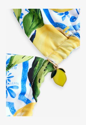 Farverigt stof med et citron- og blomstermønster, med en citroncharme i guldfarve fastgjort ved den buede kant. Glat tekstur.