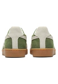 Zelené a bílé semišové tenisky s tan gumovou podrážkou, vybavené polstrovaným límcem a kontrastními panely na patě a po stranách.