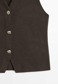 Gilet marron texturé avec un col en V, présentant des boutons métalliques et des fentes latérales pour faciliter les mouvements.