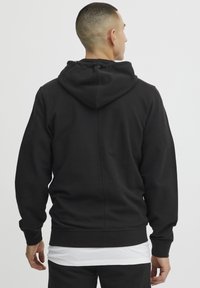 Svart hettegenser med teksturert stoff, som har kengurulomme og ribbestrikkede mansjetter. Enkelt design med medium passform.