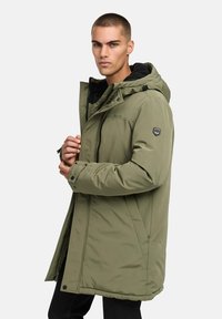 Maslinasto zeleni podstavljeni parka kaput s patentnim zatvaračem i dugmetom, podesivom kapuljačom i detaljem s logom na rukavu. Teksturirana tkanina i dugi kroj.