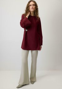 Burgundijas krāsas garās piedurknes tunika ar noapaļotu dekoltē, kurai ir dekoratīva sudraba pogca pie jostas, saskaņota ar gaišas krāsas platiem biksēm.