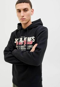 Sudadera negra con un gráfico frontal, que presenta texto en blanco y rojo. Hecha de una tela suave, tiene capucha con cordones y puños acanalados.