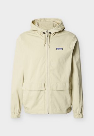 Veste à capuche beige avec fermeture éclair à l'avant, deux poches à rabat, poignets élastiques et petit logo Patagonia sur la poitrine gauche.