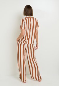 Set a due pezzi a righe nei colori ruggine e crema, composto da una maglietta a maniche corte con una vestibilità rilassata e pantaloni a gamba larga. Tessuto con una superficie liscia.
