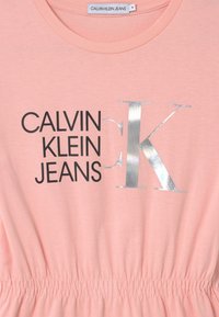 Różowa bawełniana koszulka z okrągłym dekoltem i elastycznym pasem z napisem "CALVIN KLEIN JEANS" w kolorze czarnym oraz srebrnym logiem "K".