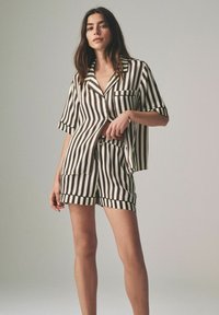 Gestreepte pyjama set in zwart-wit, kortärmige button-up overhemden met zak, bijpassende shorts met elastische taille, zachte stof textuur.
