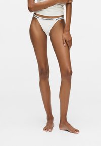 String en coton blanc avec une ceinture élastique noire portant le texte "KARL LAGERFELD". Coupe slim, design minimaliste et texture lisse.