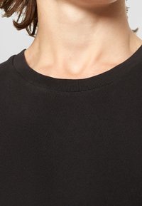 T-shirt en coton noir avec un col rond, présentant une texture côtelée et un design ajusté, mettant en valeur une surface lisse et uniforme.