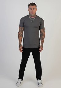 Sivá rebrovaná krátky rukáv tričko v kombinácii s čiernymi úzkymi nohavicami a bielymi teniskami. Má priliehavý strih a viditeľné tetovania na rukách.