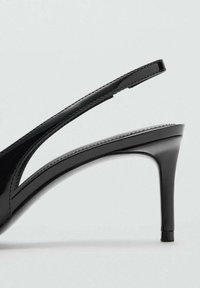 Tacón destalonado de charol negro con un elegante diseño de punta puntiaguda, un recorte curvo y un fino tacón de aguja.