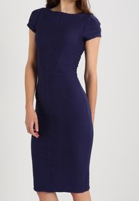 Robe midi bleu marine ajustée avec manches courtes et texture côtelée. Caractérisée par des coutures apparentes et une silhouette structurée.