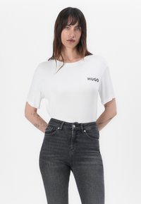 Valkoinen lyhythihainen t-paita, jossa on musta "HUGO"-logo. Parit korkea vyötäröinen musta farkut, joissa on viisi taskua ja hienovarainen tekstuuri.