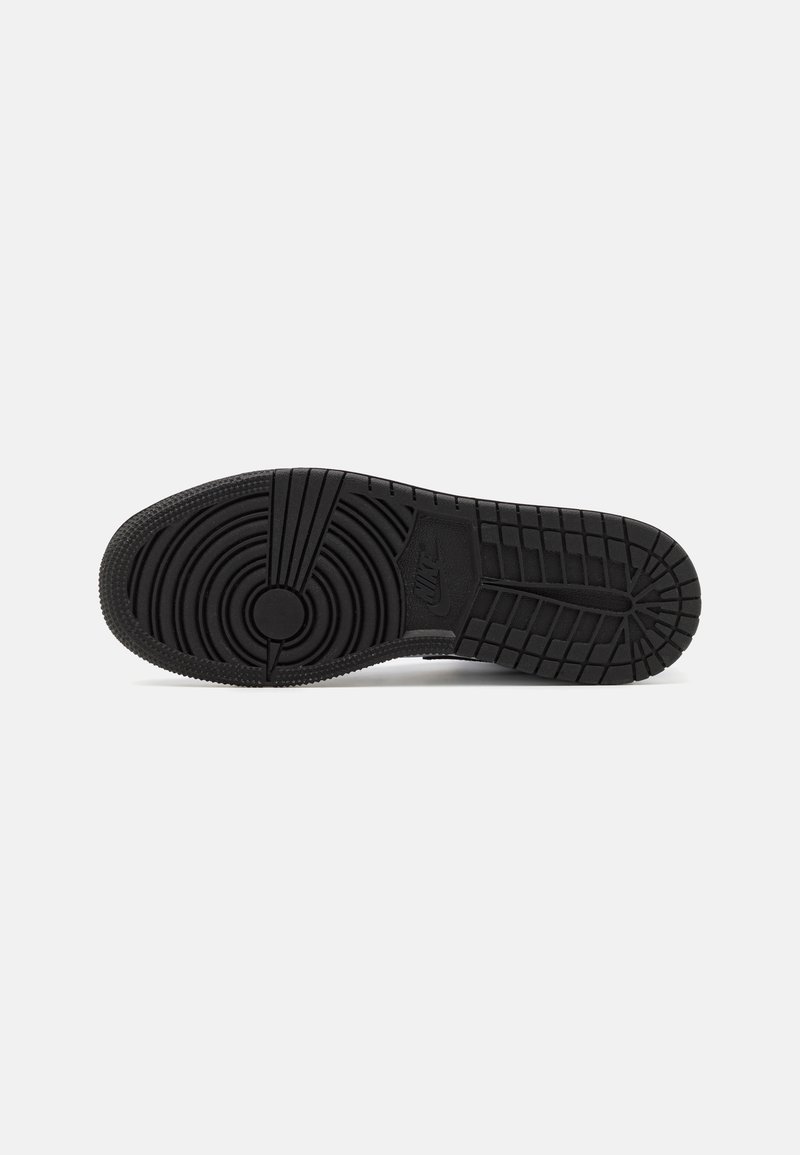 Suela de zapatilla negra con patrones de tracción circulares y lineales. Material de goma texturizada con un detalle de logo prominente. Forma plana y ancha.
