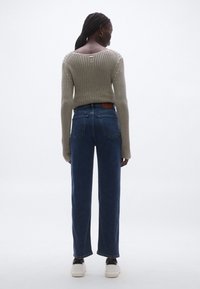 Kötött bézs pulóver széles nyakkivágással, magasderekú kék farmerral párosítva. Fehér tornacipővel és barna bőr címkével a farmernadrágon kiegészítve.