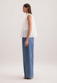 Top bianco senza maniche con dettagli a occhio di pernice, orlo ondulato e vestibilità rilassata, abbinato a una gonna in denim azzurro chiaro a vita alta. Tacchi neri.