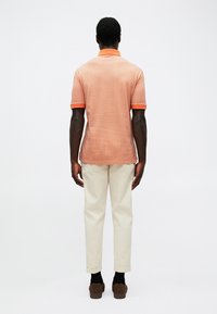 Polo shirt portocalie cu maneci scurte, cu un model texturat și guler contrastant, asociat cu pantaloni bej deschis, rulati, și pantofi maro.