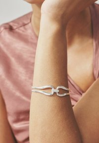 Bracciale d'argento con design intrecciato, caratterizzato da una sezione centrale texturizzata. Finitura liscia e un aspetto elegante e moderno.