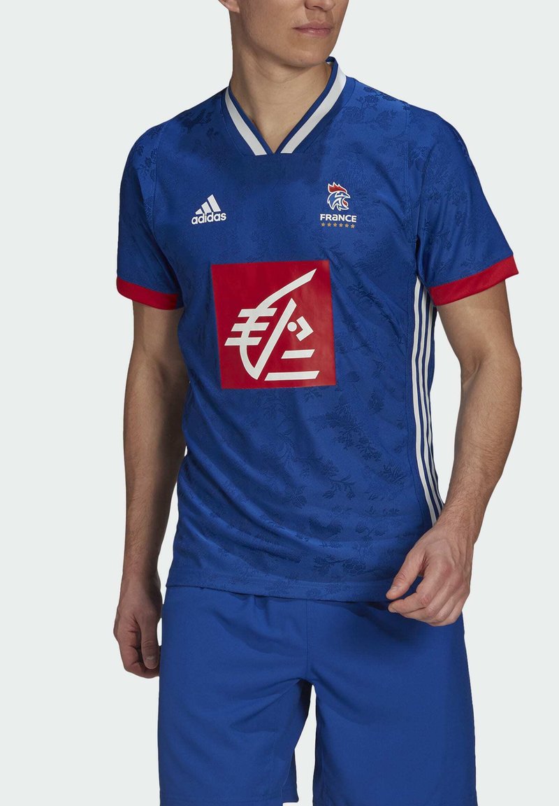 Blauw voetbalshirt met rode accenten, bloemenpatroon, Adidas-logo en Frankrijk-embleem; ronde hals en korte mouwen; gecombineerd met blauwe shorts.