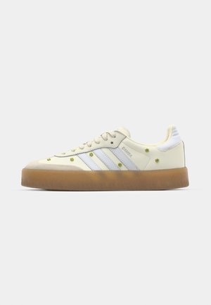 Kremfargede sneakers med lyseblå striper, gummisåle og dekorative gule blomstdetaljer på overmaterialet. Rundt tådesign.