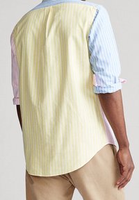 Koszula z kołnierzykiem w wielokolorowe paski w odcieniach pastelowych: żółtym, niebieskim i różowym, z podwiniętymi rękawami i luźnym krojem. Wykonana z bawełny, widok z tyłu.