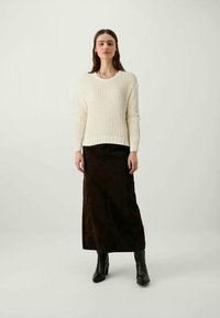 Suéter de punto de color crema claro con cuello redondo y dobladillo acanalado, combinado con una falda maxi de pana marrón oscura y botas negras hasta el tobillo.