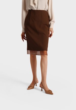 Gonna a matita marrone con due tasche frontali, dettaglio orlo trasparente e design aderente, abbinata a scarpe con tacco marroni con accenti circolari.