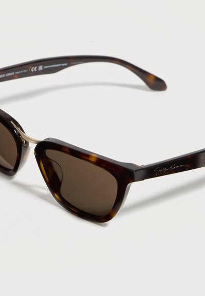 Ορθογώνια γυαλιά ηλίου ταρταρούγα με σκουρα φακούς και γεφυράκι και λεπτομέρειες από μεταλλικό χρυσό τόνο, ακουμπισμένα σε λευκή επιφάνεια.