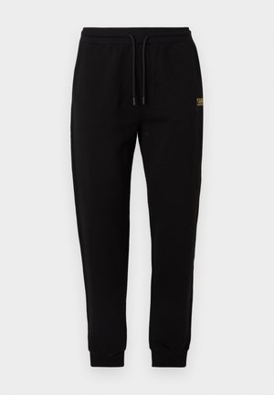 Schwarze Jogginghose mit elastischem Bund, Kordelzug, Bündchen an den Knöcheln und kleinem goldenem Logo am oberen linken Oberschenkel.