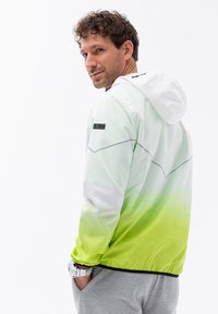 Giubbotto leggero in gradiente bianco-verde, con cappuccio e accenti grigi. Realizzato in un materiale liscio e lucido, con una vestibilità comoda.