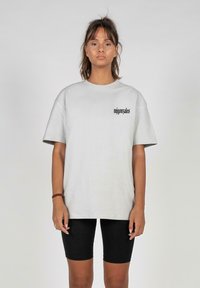 Light grey oversized t-shirt in cotton, featuring a black logo on the left chest. Short sleeves, round neckline, paired with black shorts.