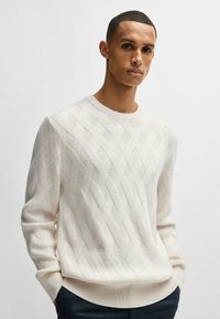 Maglione a maglia color crema con un motivo a diamante testurizzato, scollo rotondo e polsini e orlo a coste. Tessuto leggero e traspirante.
