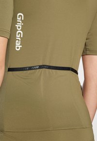 Camiseta deportiva de un verde oliva con mangas texturizadas y banda negra en la cintura. Presenta el logo "GripGrab" en blanco.