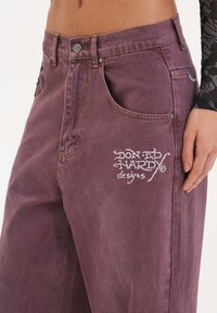 Lila denimjeans med hög midja, framfickor och broderad "Don Ed Hardy designs" logotyp. Slät textur med subtila sömdetaljer.