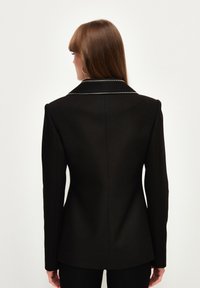 Schwarz maßgeschneiderter Blazer mit scharfem Kragen, strukturierten Schultern und einer Ein-Knopf-Verschluss. Glattes Gewebe mit einer eleganten Oberfläche.