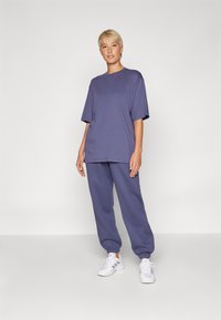 T-shirt surdimensionné à col rond et joggers assortis en tissu violet doux. Coupe décontractée avec des poignets élastiques et un design simple. Baskets blanches.