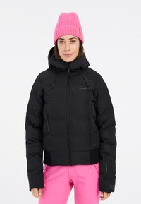 Schwarze Pufferjacke mit Kapuze, ausgestattet mit Reißverschlusstaschen vorne und elastischen Bündchen. Kombiniert mit leuchtend pinkfarbenen Hosen und einer strukturierten pinken Mütze.