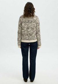 Strickpullover in Creme und Braun mit einem strukturierten Muster, langärmlig und mit geripptem Saum. Kombiniert mit dunkelblauen, weit ausgestellten Jeans.