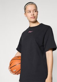 Black cotton t-shirt with short sleeves, featuring a pink Nike logo on the chest. The person holds an orange basketball.
