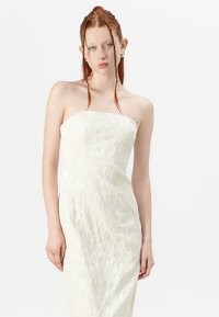 Uten ermer kremfarget kjole med blomsterbroderi, tettsittende silhuett og jevn tekstur. Stoffet ser lett ut med subtil glans.
