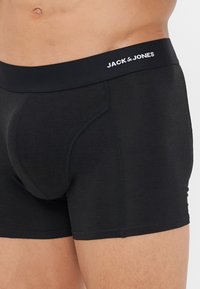 Boxers noirs avec une large ceinture élastique arborant le texte "JACK & JONES" en blanc. Le tissu a une texture lisse et un design ajusté.